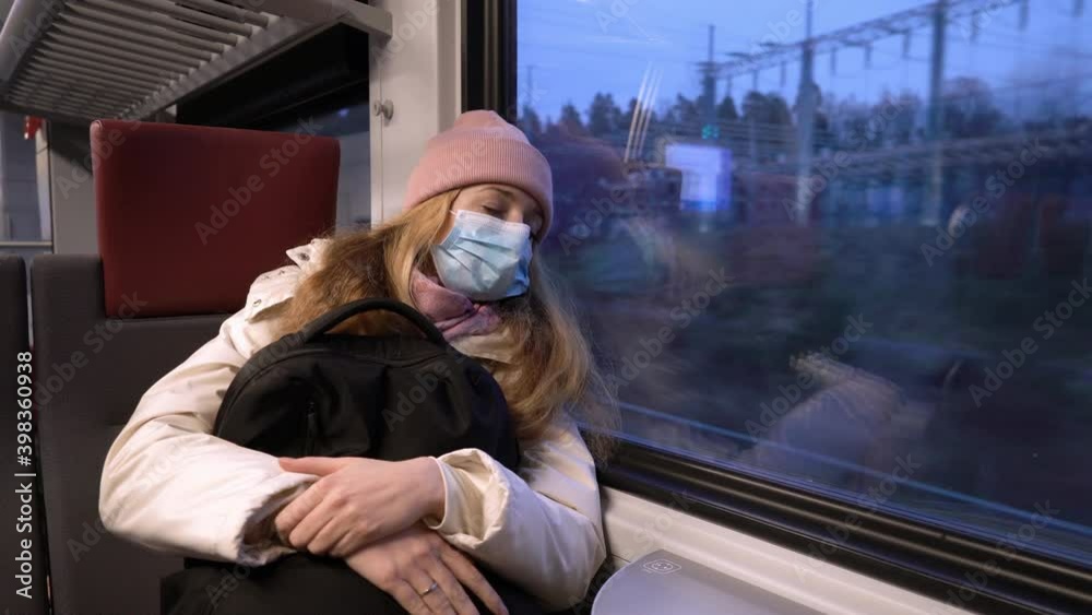 Traveling on public transport during the pandemic. Tired woman in medical protective mask sleeping in commuter train. Traveling on public transport during the pandemic. Tired woman in medical protective mask sleeping in commuter train.