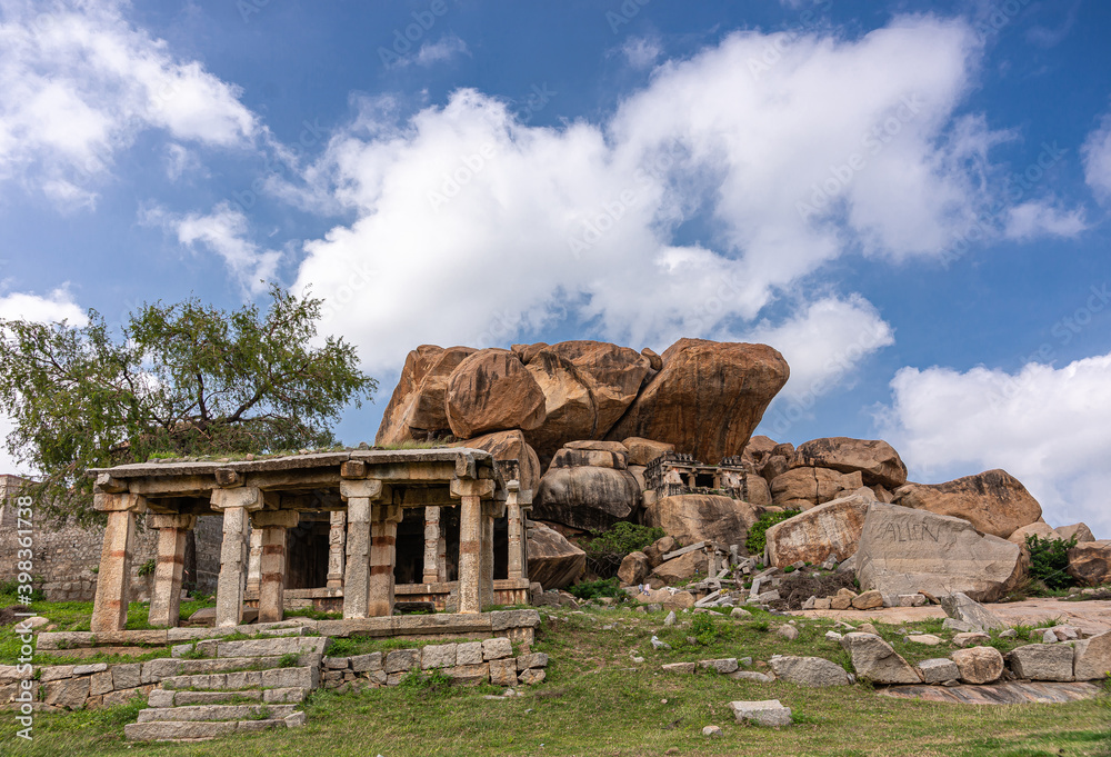 Hampi, Karnataka, India - November 4, 2013: Ruinous Kadelekalu Ganesha temple. smaller mandapam and shrine under huge boulders and blue cloudscape.
