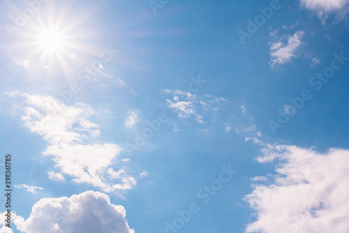 View of the blue sky with white cumulus clouds and the bright sun with rays and highlights.