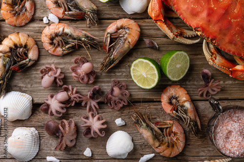 View from above of crab, shrimps and octopuses served with lime on wooden background. Delicious meal. Concept of assorted seafood. Food banner. Islands cuisine.