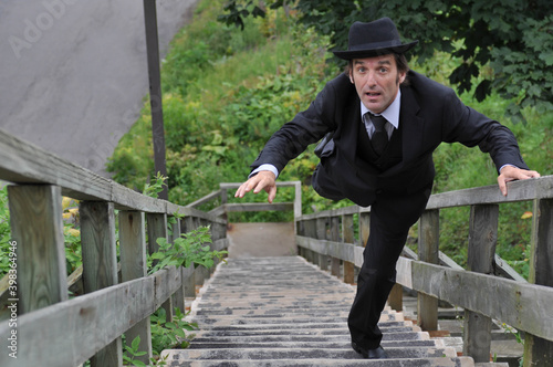 Businessman in a black suit and black hat ruining up old wooden stairs or falling down the stairs