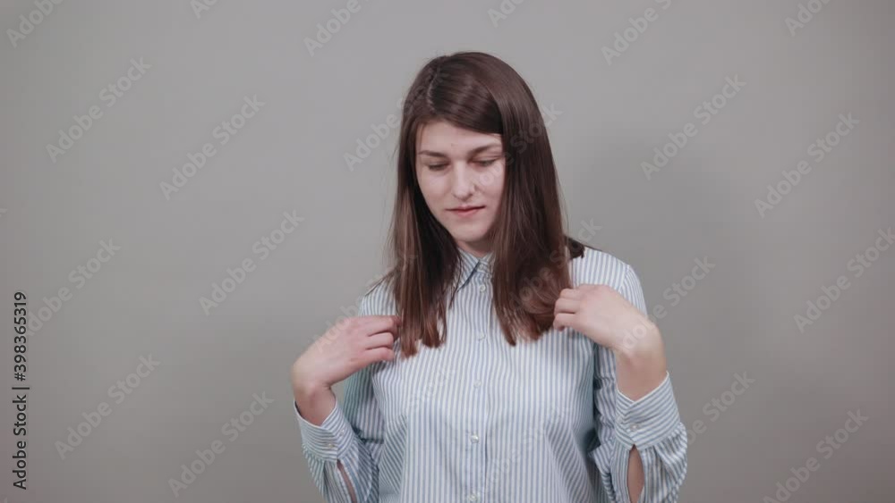 Pointing with hand at chest and staring. Shocked facial expression. Young attractive woman, dressed blue shirt with brown eyes, brunette hair, grey background Pointing with hand at chest and staring. Shocked facial expression. Young attractive woman, dressed blue shirt with brown eyes, brunette hair, grey background