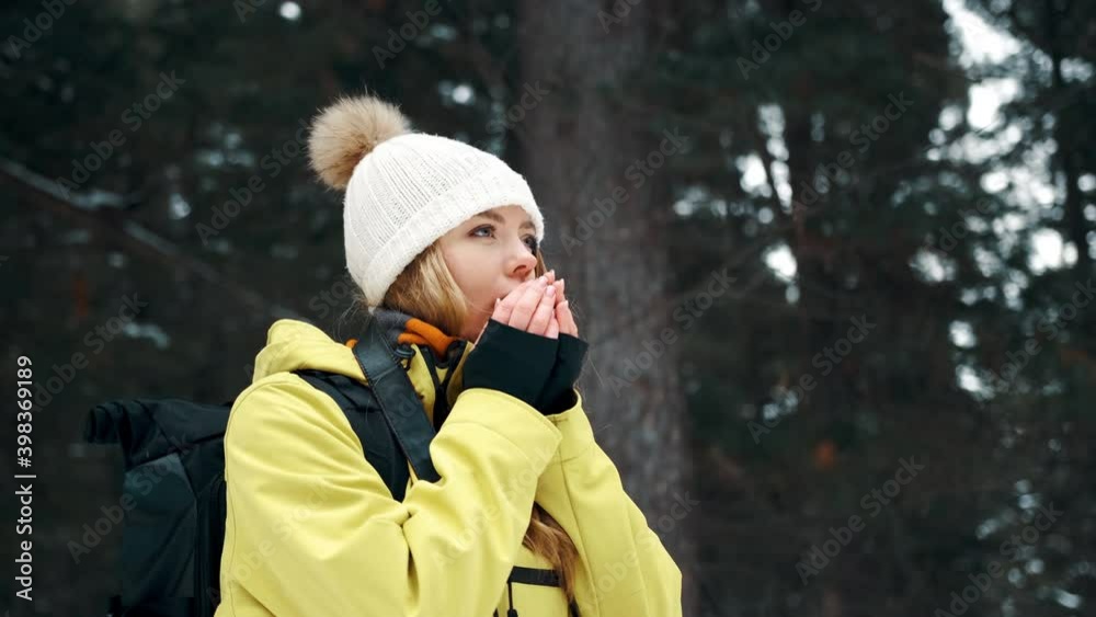 A girl in a white hat and a yellow anorak warms her hands in the winter in the forest A girl in a white hat and a yellow anorak warms her hands in the winter in the forest