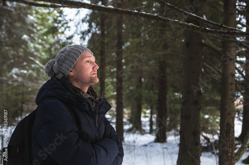 Young Man Backpacker In Winter Snowy Forest. Active Hobby. Hiker Walking In Snowy Pinewood Forest. Copy space.