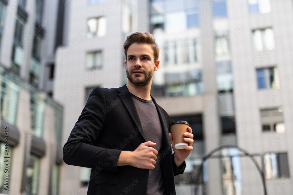 Business, hot drinks and people and concept - young serious businessman with paper coffee cup over office building Business, hot drinks and people and concept - young serious businessman with paper coffee cup over office building