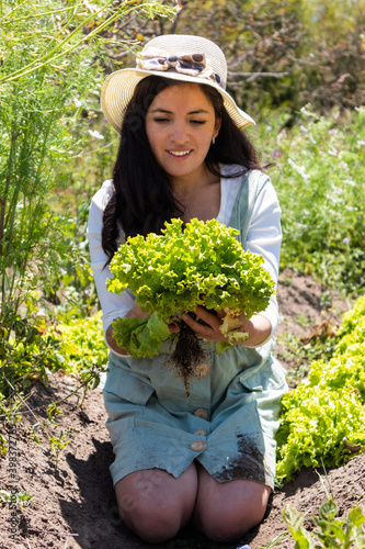 Young woman holding and admiring in her hands a lettuce that she just harvested