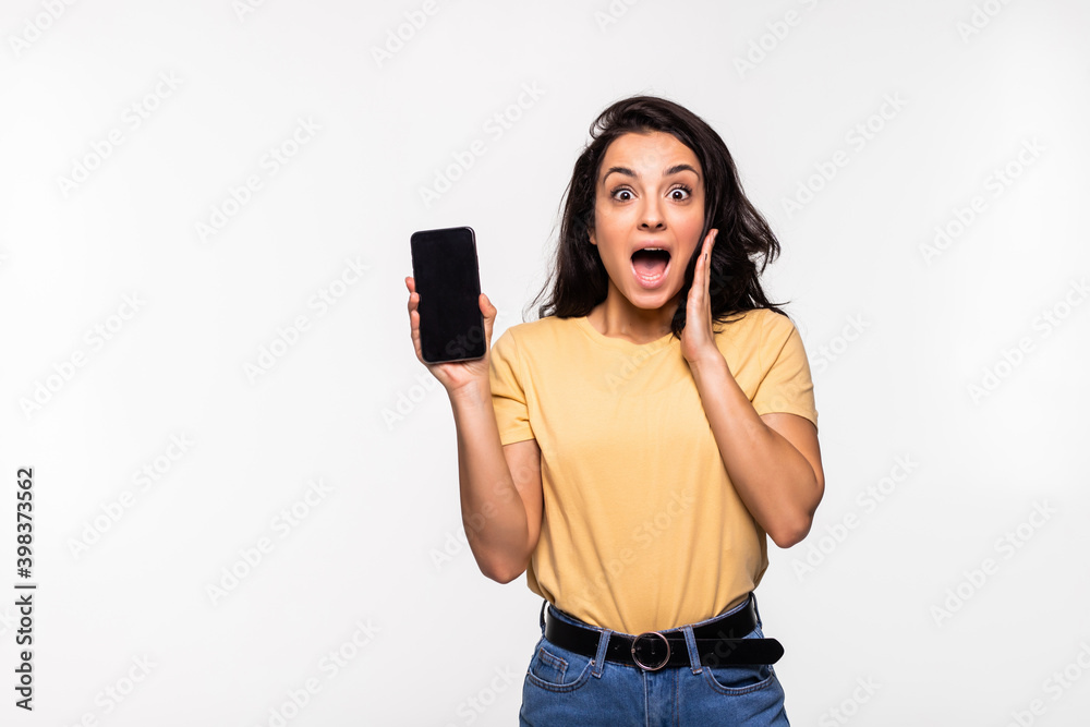 Shocked young woman holding mobile phone with blank empty screen in white shirt posing isolated on white background. Achievement career wealth business concept. Shocked young woman holding mobile phone with blank empty screen in white shirt posing isolated on white background. Achievement career wealth business concept.