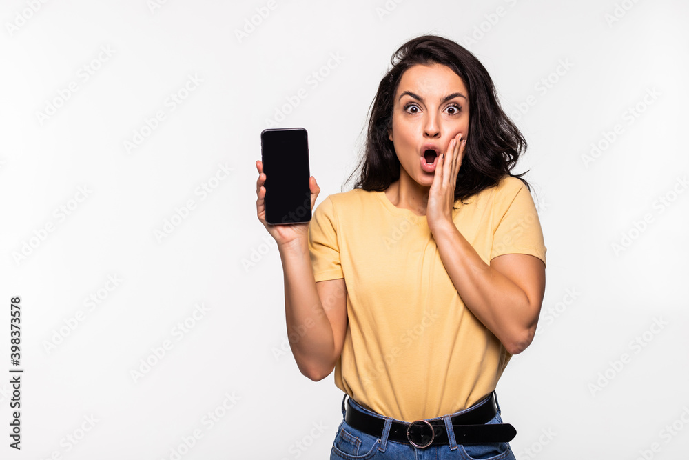 Shocked young woman holding mobile phone with blank empty screen in white shirt posing isolated on white background. Achievement career wealth business concept. Shocked young woman holding mobile phone with blank empty screen in white shirt posing isolated on white background. Achievement career wealth business concept.
