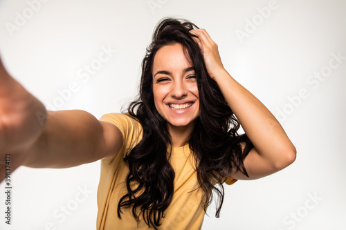 Beautiful young woman is making selfie photo with smartphone isolated white background
