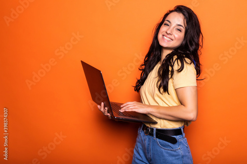 Smiling young blonde woman holding laptop posing isolated on yellow orange background. People lifestyle concept.