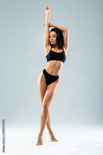 Full heaight of young beautiful woman body on gray background in black sport clothes