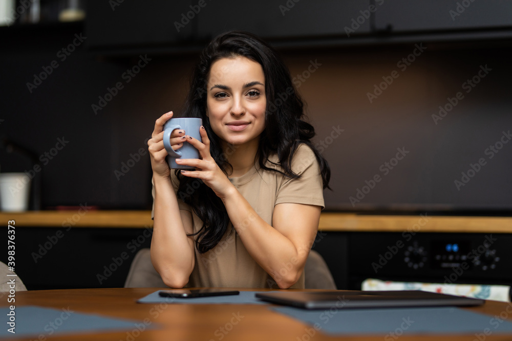 Relaxed young woman drinking coffee in kitchen and looking out the window Relaxed young woman drinking coffee in kitchen and looking out the window