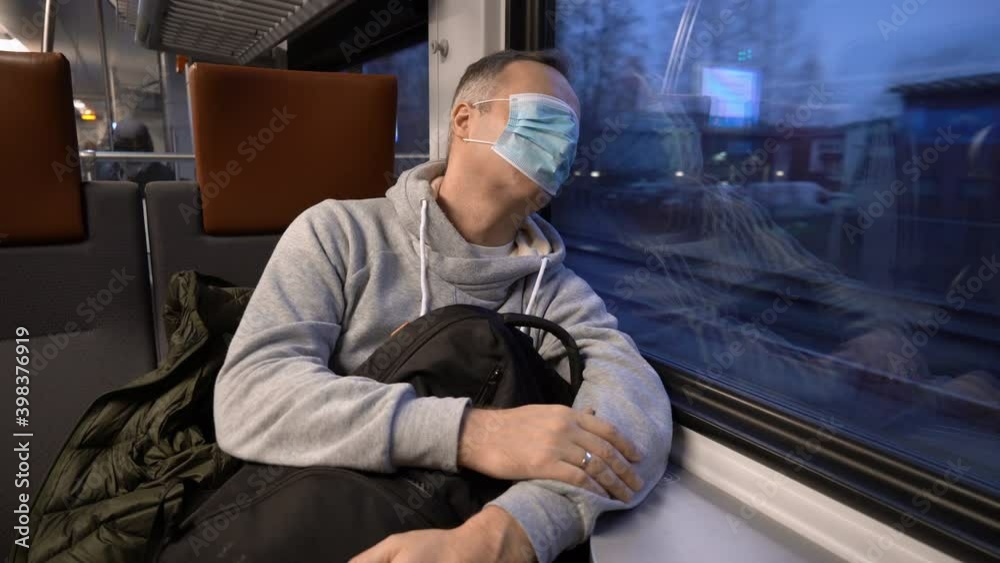 Traveling on public transport during the pandemic. Tired middle aged man wearing medical protective mask on his eyes sleeping in commuter train.
