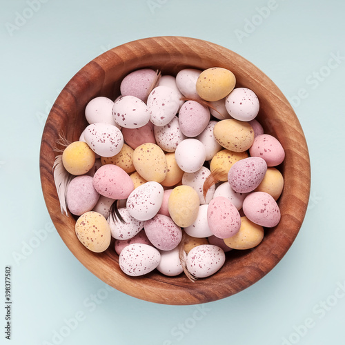 Easter eggs in wooden bowl on blue background. Square format. Top view. White yellow pink eggs for Easter treat.