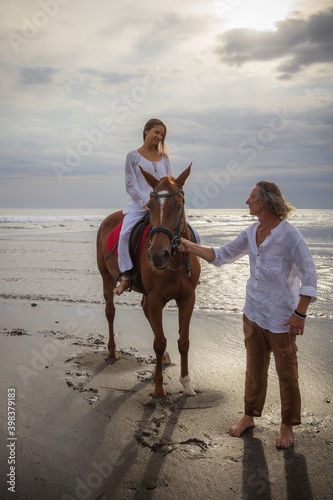 Horse riding on the beach. Woman on a brown horse. Man leading horse by its reins. Love to animals. Husband and wife spending time together. Selected focus.