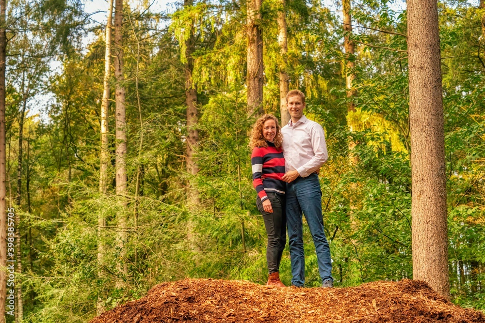 Tall boy and smaller girl they are standing on a mountain of bark in the forest, looking at the camera