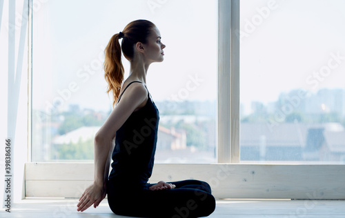 Free Download Woman practices yoga and hands behind her back crossed legs by window room - GFXLoad