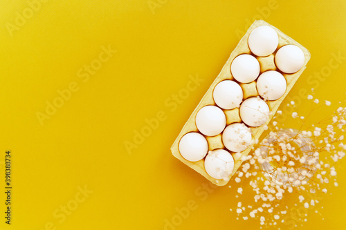 raw shell eggs pack flat lay illuminate yellow background, white sprind flowers, easter holiday photo