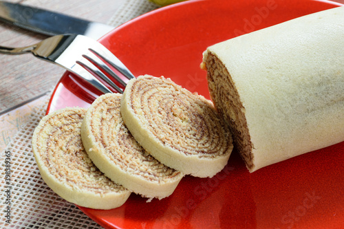 Closeup of sliced bolo de rolo (roll cake) on a red plate next to a fork. photo