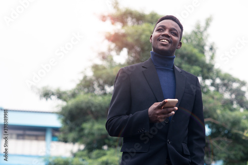 Handsome african business man using smartphone in trendy formal black suit. Guy with beard wearing blue long sleeve or sweater