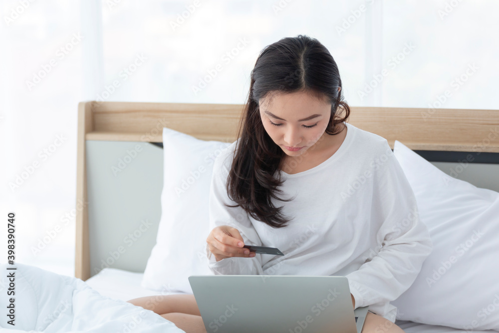 Woman sitting on the bed, shopping online with notebook. Happy casual beautiful woman working on a laptop sitting on the bed at home. Woman sitting on the bed, shopping online with notebook. Happy casual beautiful woman working on a laptop sitting on the bed at home.