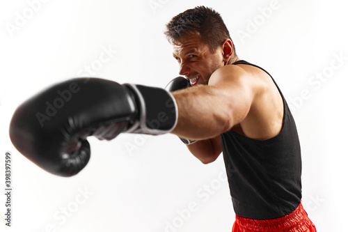 sporty man in black boxing gloves hitting at camera isolated on white background. © producer
