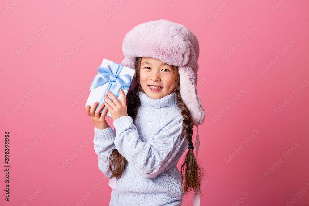 Cute little Asian girl in a winter hat and sweater holds a gift box. Christmas concept, text space Cute little Asian girl in a winter hat and sweater holds a gift box. Christmas concept, text space