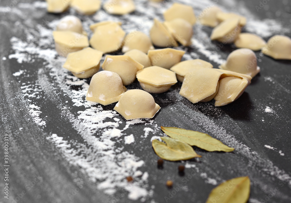 The background is a black table, sprinkled with flour, smeared by hand, on it are dumplings, in the center are bay leaves and peppercorns.