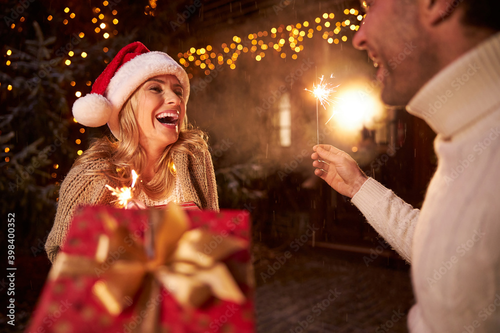 Happy smiling sweet couple in warm clothes with sparklers in hands spending great time near home Happy smiling sweet couple in warm clothes with sparklers in hands spending great time near home