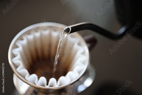 Barista making coffee with a pour over coffee maker in a dripper and pouring hot water from a black pot on a macro scale