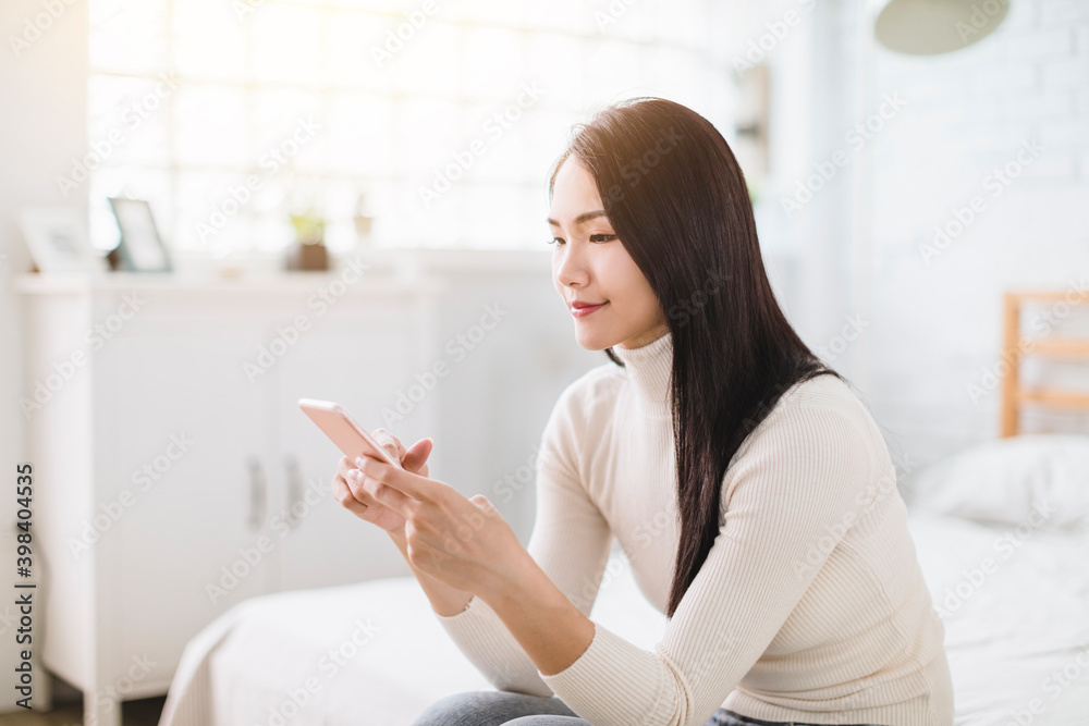 Young woman sitting in bedroom and using smartphone Young woman sitting in bedroom and using smartphone