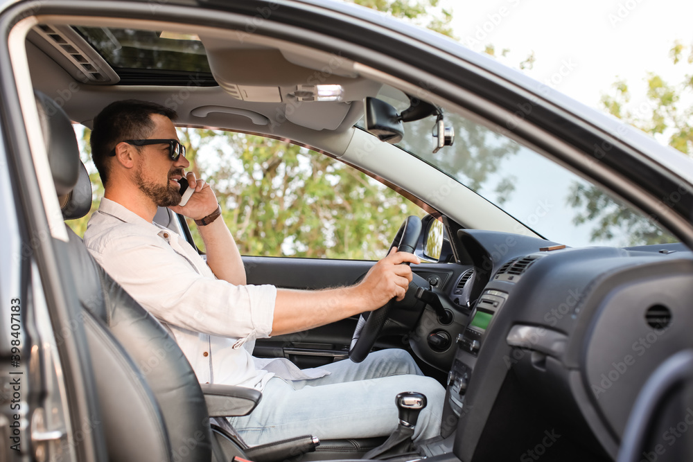 Handsome man talking by mobile phone in modern car