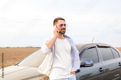 Handsome man talking by mobile phone near his modern car