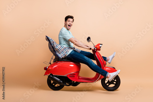 Profile side view portrait of nice funky cheerful guy driving moped fooling having fun fast speed isolated over beige pastel color background © deagreez