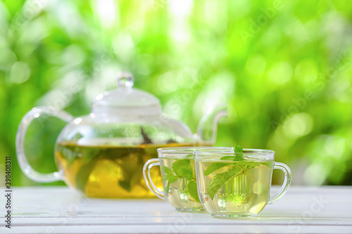 Teapot and cups of green tea with mint on blurred background