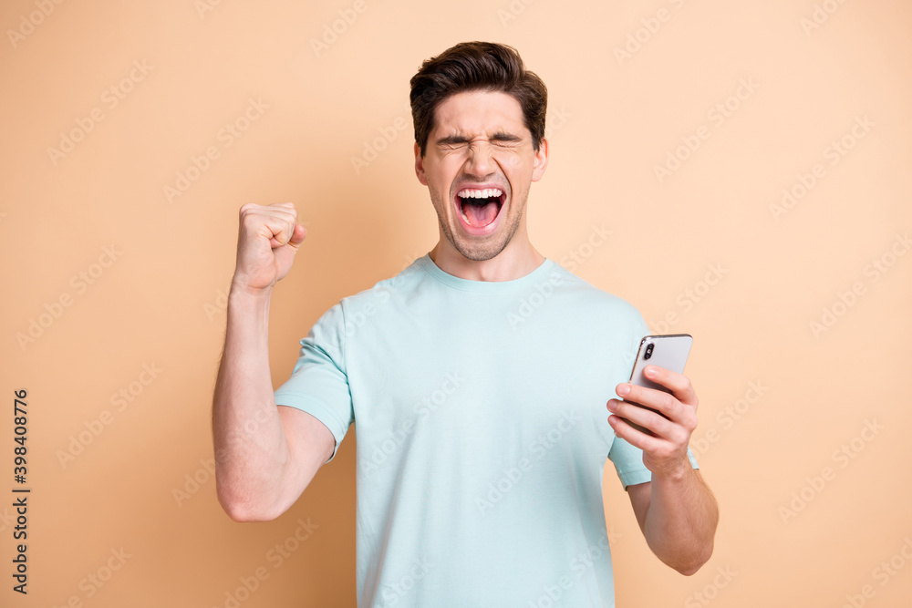 Portrait of nice cheerful overjoyed guy influenzer using device having fun rejoicing smm isolated over beige pastel color background Portrait of nice cheerful overjoyed guy influenzer using device having fun rejoicing smm isolated over beige pastel color background