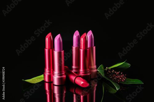 Different lipsticks and flower on black background