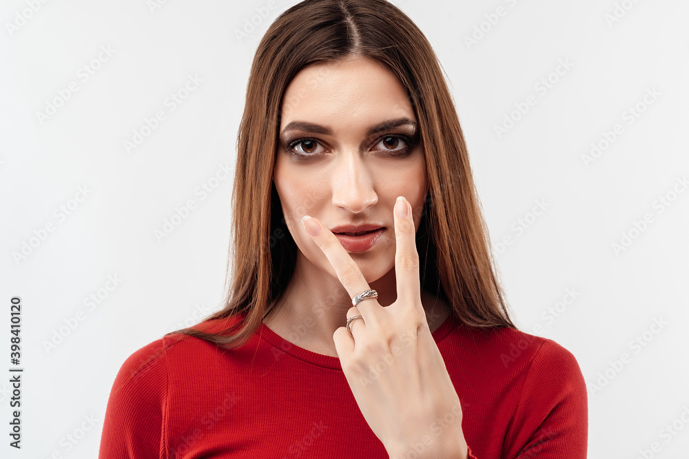 Beautiful brunette in casual red sweater point to the eyes. Studio shot, white background. Human emotions concept Beautiful brunette in casual red sweater point to the eyes. Studio shot, white background. Human emotions concept