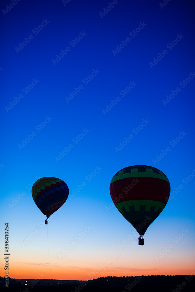 Fototapeta premium Two Colorful Air Balloons Levitating Over the Field Outdoors Against Clear Blue Skies At Twilight.
