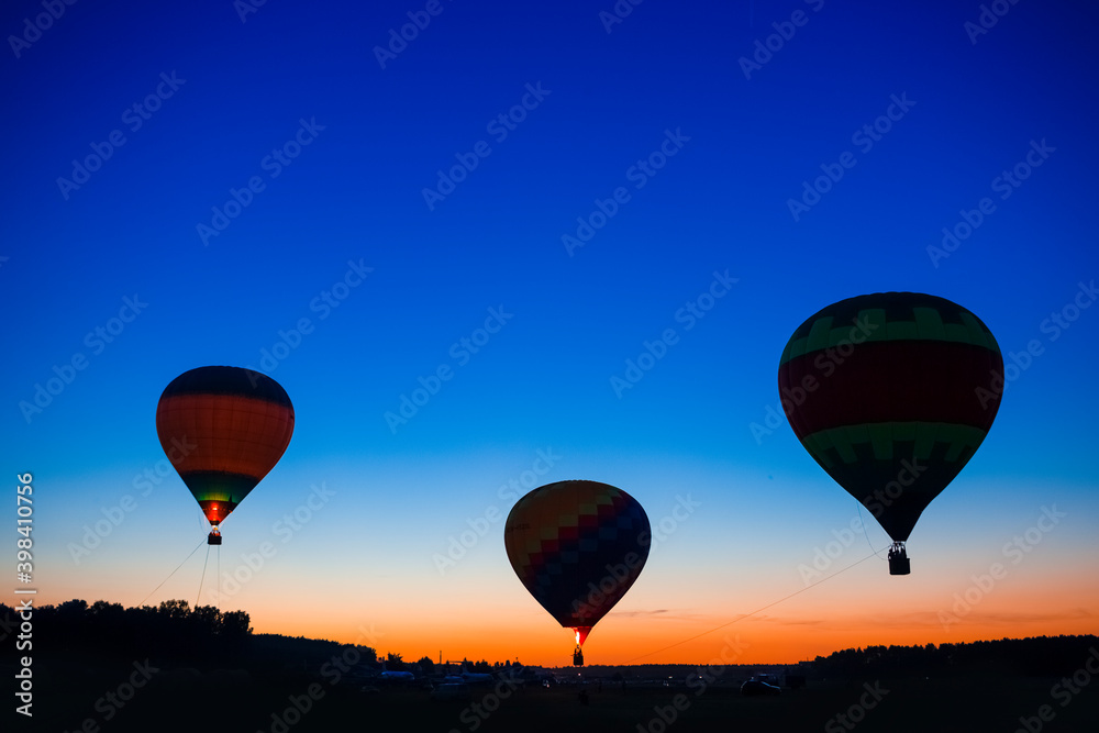 Three Amazing Colorful Air Balloons Levitating Over the Ground Outdoors Against Clear Blue Skies At Twilight.