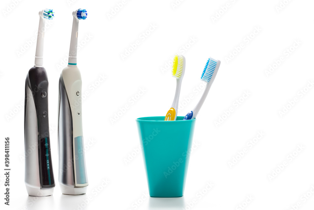Pair of Professional Electric Toothbrushes In Front of Two Manual Tooth Brushes in One Cup On White Pair of Professional Electric Toothbrushes In Front of Two Manual Tooth Brushes in One Cup On White