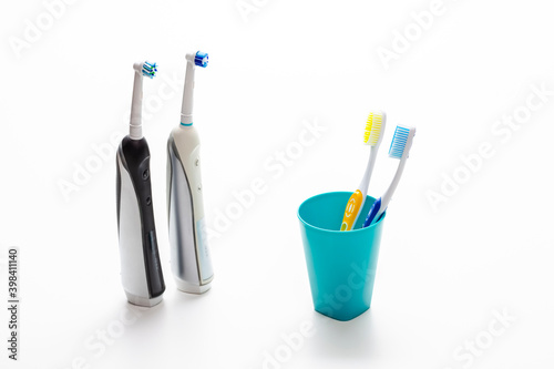 Professional Electric Toothbrushes In Front of Two Manual Tooth Brushes in One Cup On White