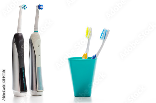 Pair of Professional Electric Toothbrushes In Front of Two Manual Tooth Brushes in One Cup On White