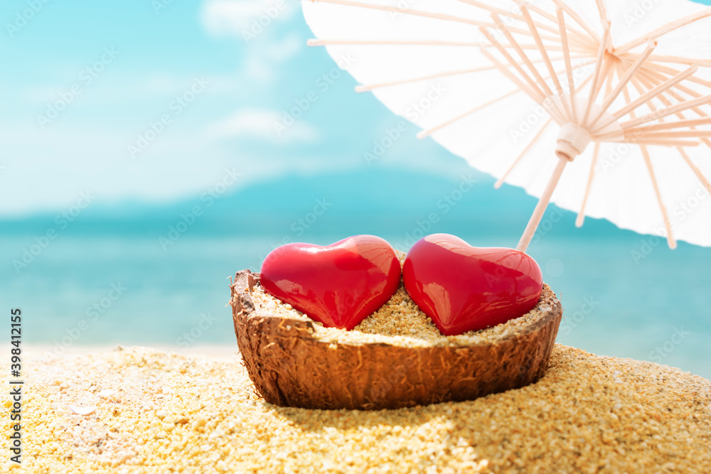 Two red hearts under beach umbrella, blue sky and sea in background. Romantic trip for love couple concept. Valentines Day, 14 February symbol. Copy space Two red hearts under beach umbrella, blue sky and sea in background. Romantic trip for love couple concept. Valentines Day, 14 February symbol. Copy space