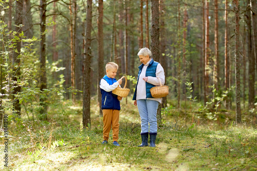 picking season, leisure and people concept - happy smiling grandmother and grandson with baskets and mushrooms in forest