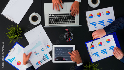 Top view of office workers discussing business financial diagrams and working on digital devices. Working in team conference with project planning document and modern technology on company table.