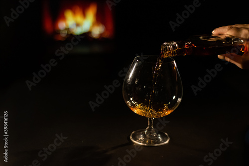 Close-up of a female hand with a glass of brandy on the background of the fireplace