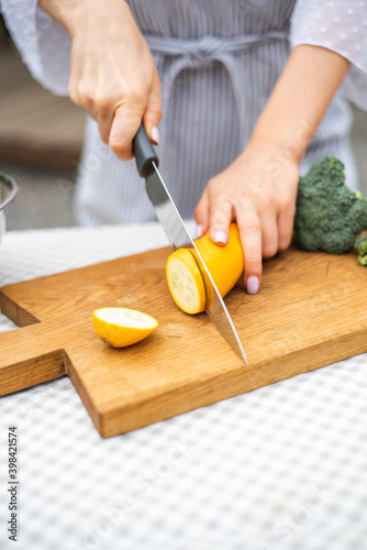 Female hands cut with knife young seasonal zucchini into slices on wooden cutting board. Sliced zucchini. The method of preparation of vegetables. Seasonal products, harvest. Healthy nutrition, diet.