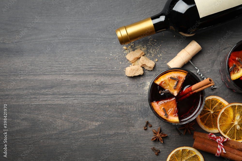Bottle of wine, cup of mulled wine and ingredients on wooden background