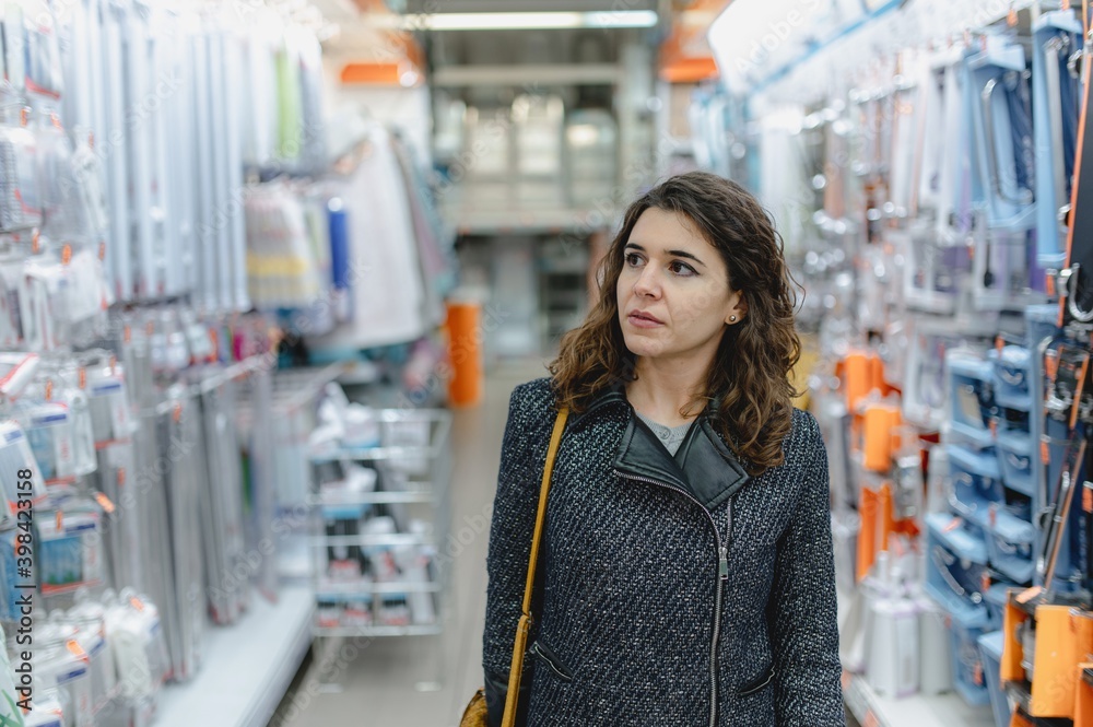Close-up young caucasian woman portrait walking in the shelf store. Serious and concentrate lady looking the woods. Buy concept. Close-up young caucasian woman portrait walking in the shelf store. Serious and concentrate lady looking the woods. Buy concept.